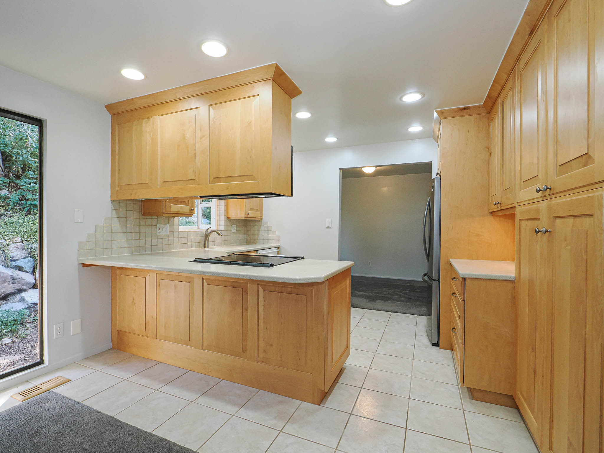 Kitchen featuring light wood cabinetry, recessed lighting, tile flooring, built-in cooktop, and a stainless steel refrigerator