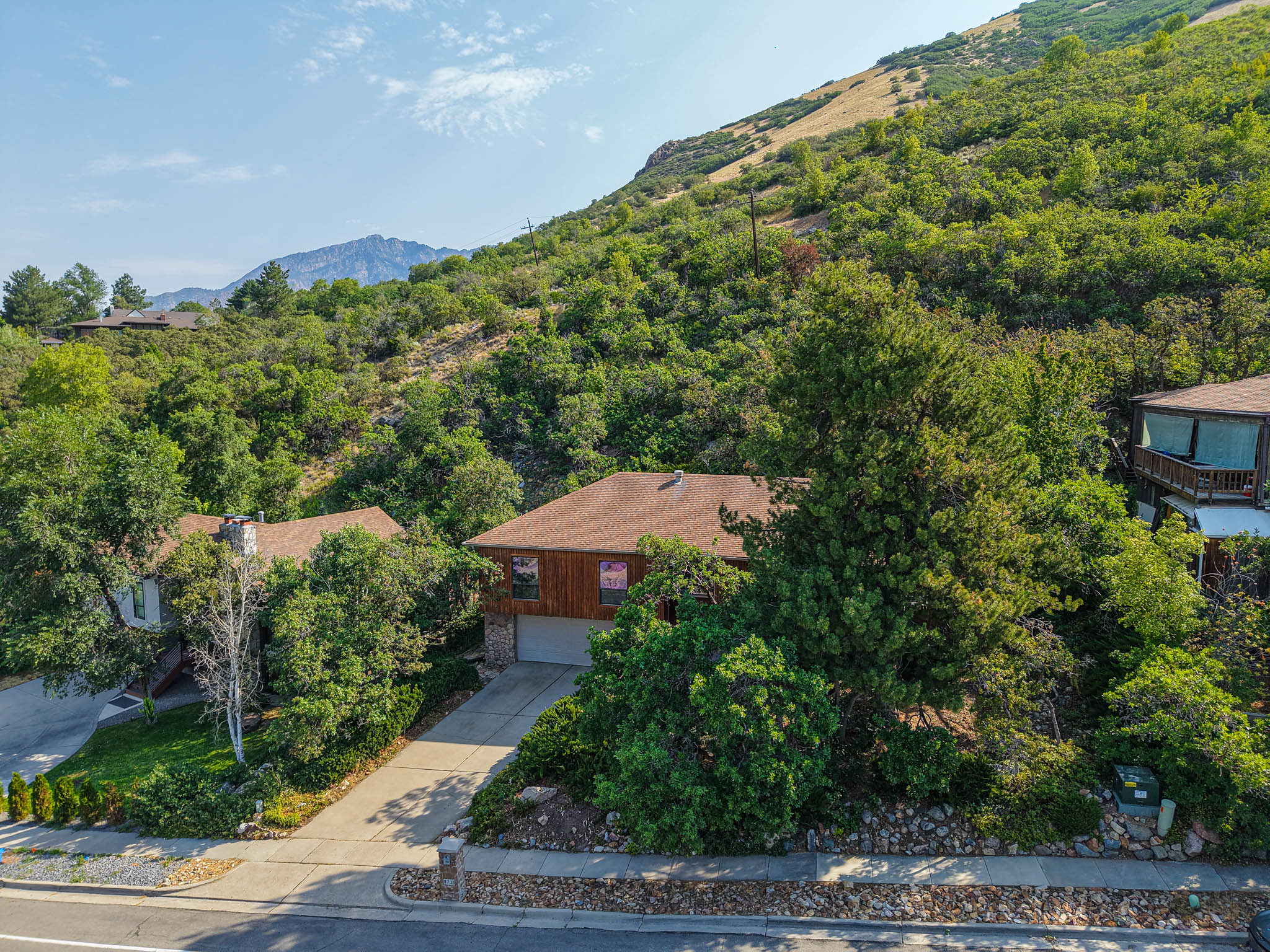 Wood-sided home with a brown shingled roof, featuring a paved driveway and an integrated garage