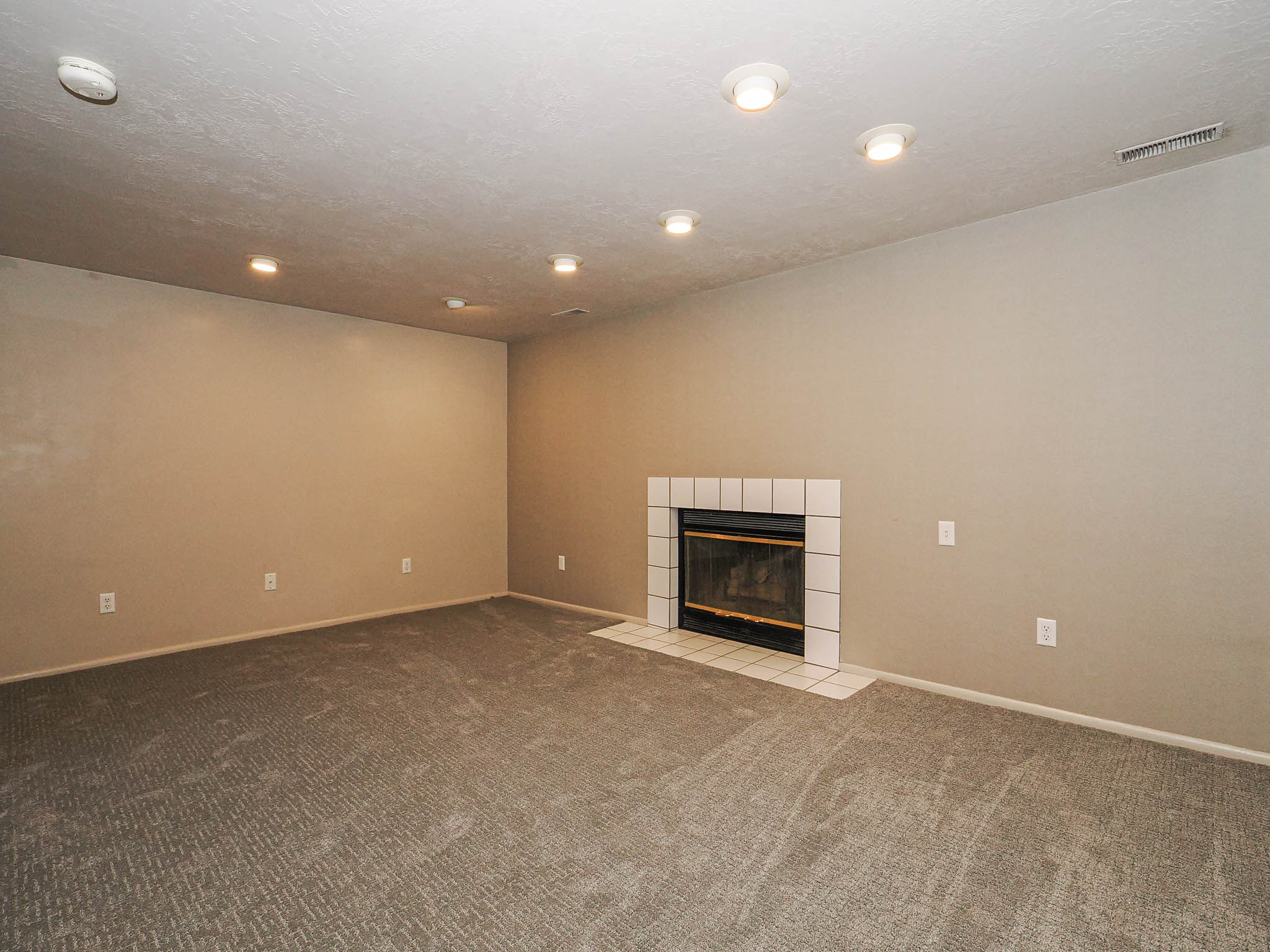 Spacious room featuring a fireplace with white tile surround, recessed lighting, neutral wall color, and textured carpeting