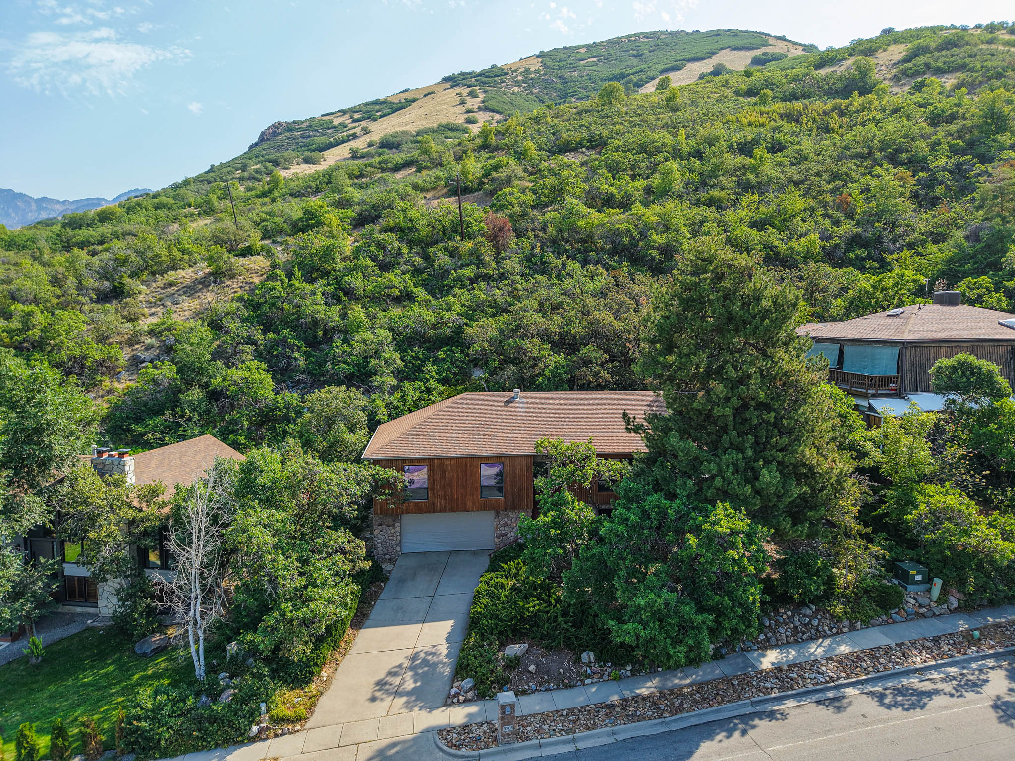 Wood-sided residence featuring a stone-clad lower level, integrated garage, and a sloped roofline