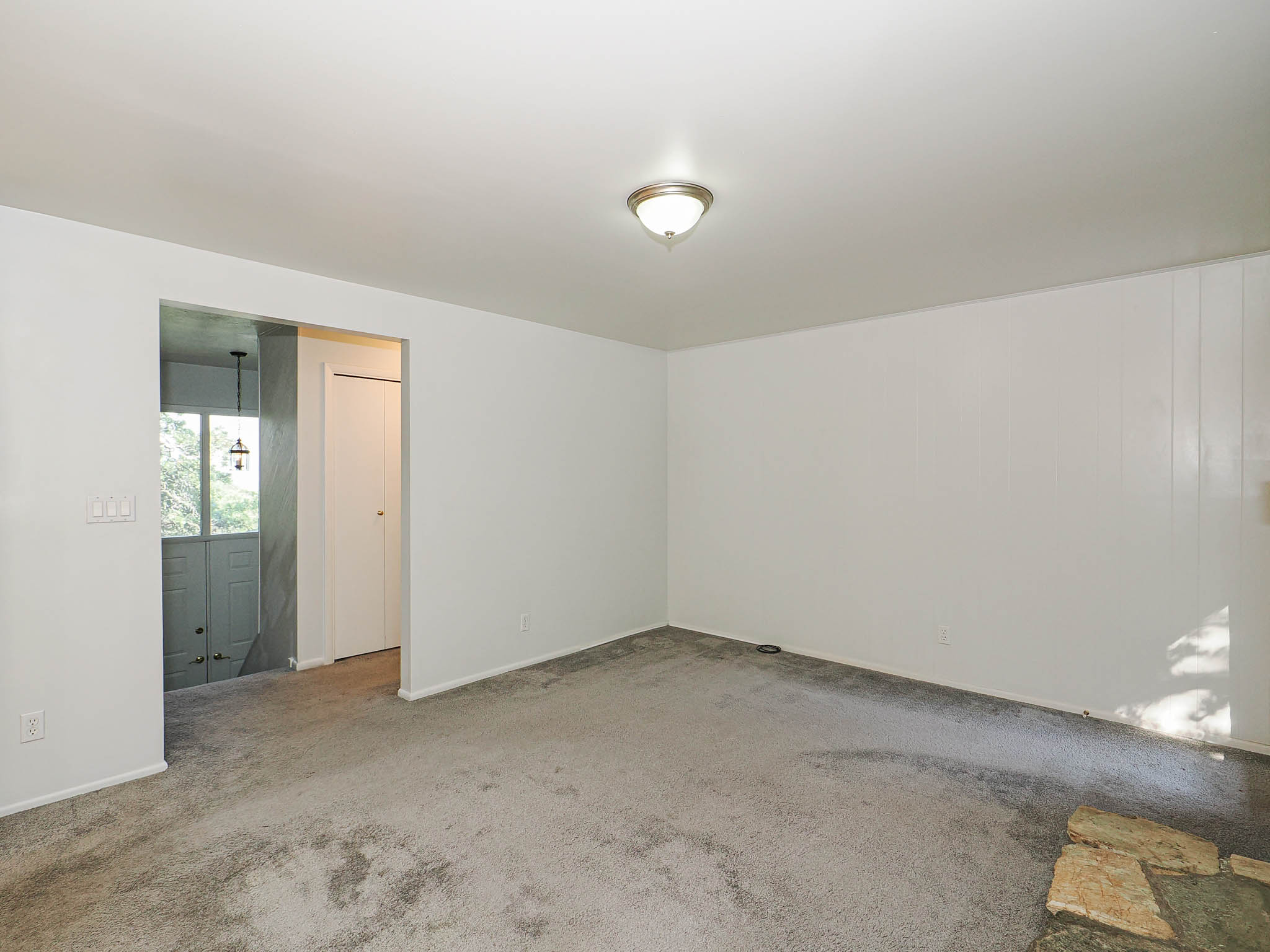 Spacious room featuring neutral carpeting, white painted walls, and an overhead flush-mount light fixture