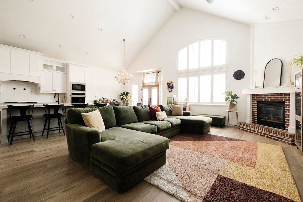 Integrated kitchen and living area featuring vaulted ceilings, wood-finish flooring, and an exposed brick fireplace