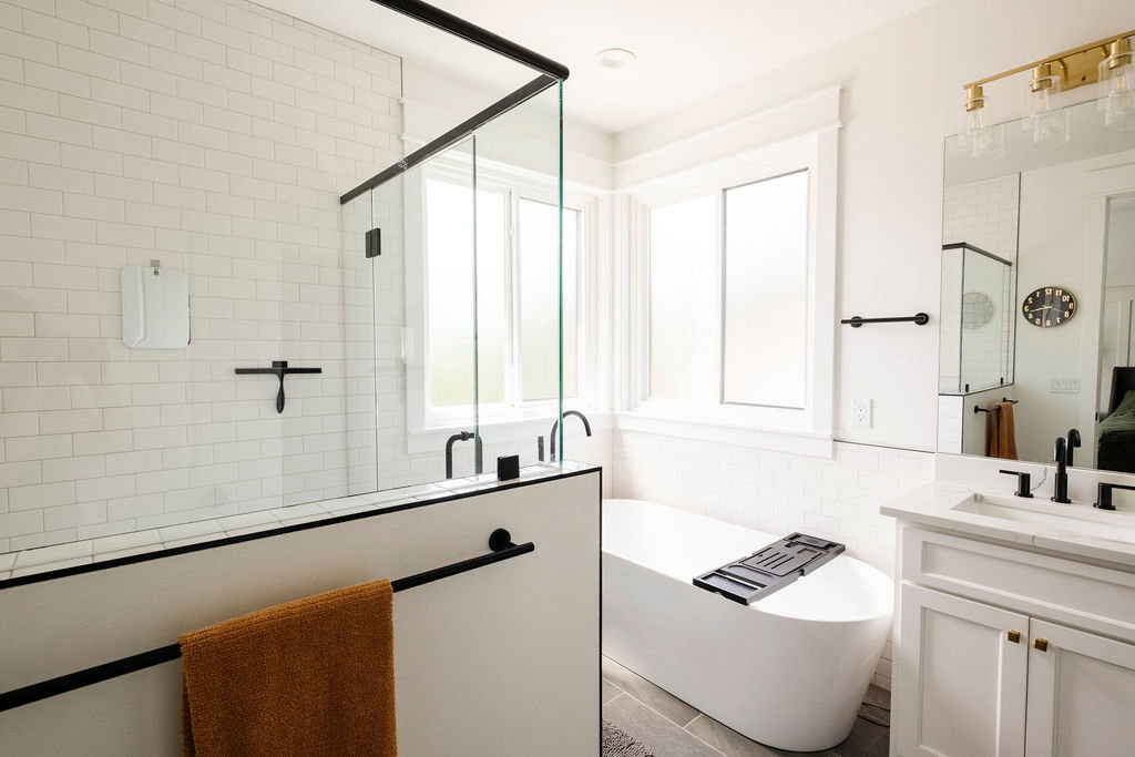 Bathroom featuring a frameless glass shower enclosure with matte black trim, a freestanding soaking tub, a single vanity with a white countertop, a large mirror, and matte black fixtures