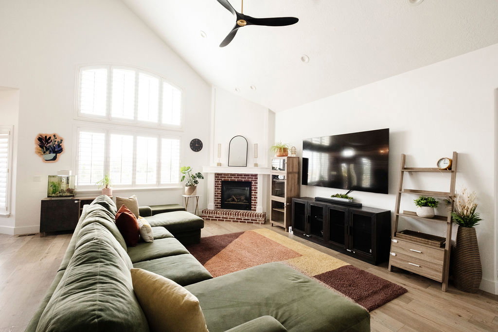 Spacious living area featuring a vaulted ceiling, light wood-finish flooring, and a brick-surround fireplace with a mantel
