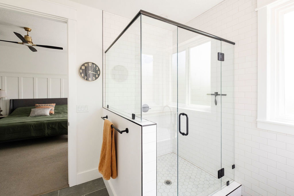 Glass-enclosed shower featuring black-framed clear glass panels, white subway tile walls, and a hexagonal tile floor