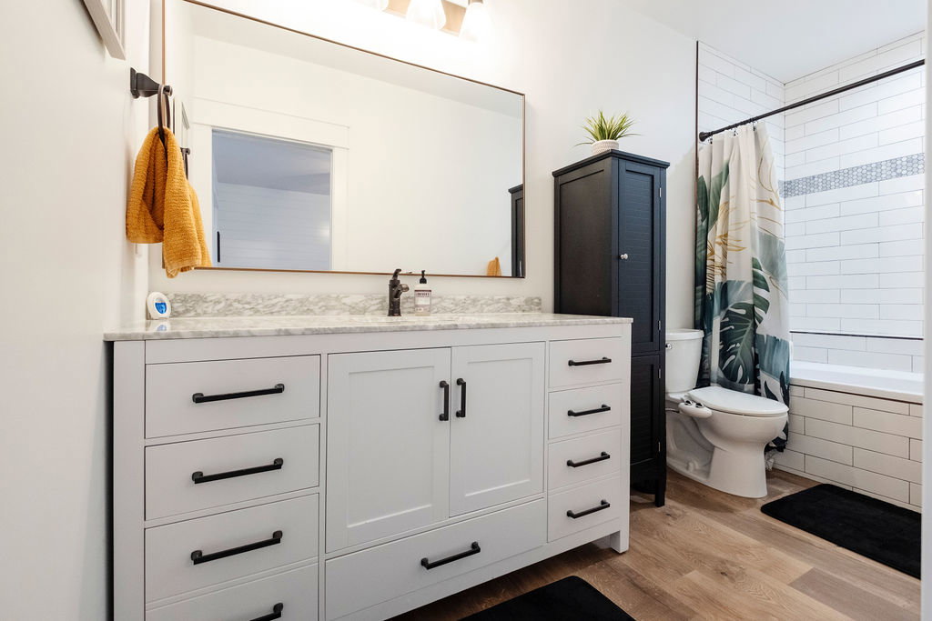 Bathroom featuring a white vanity with a light-colored countertop, matte black hardware, and wood-finish flooring
