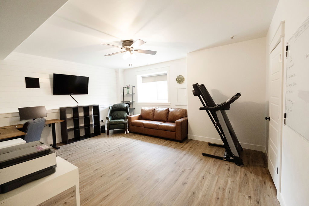 Spacious room featuring wood-finish flooring, a ceiling fan, and white walls with a shiplap accent