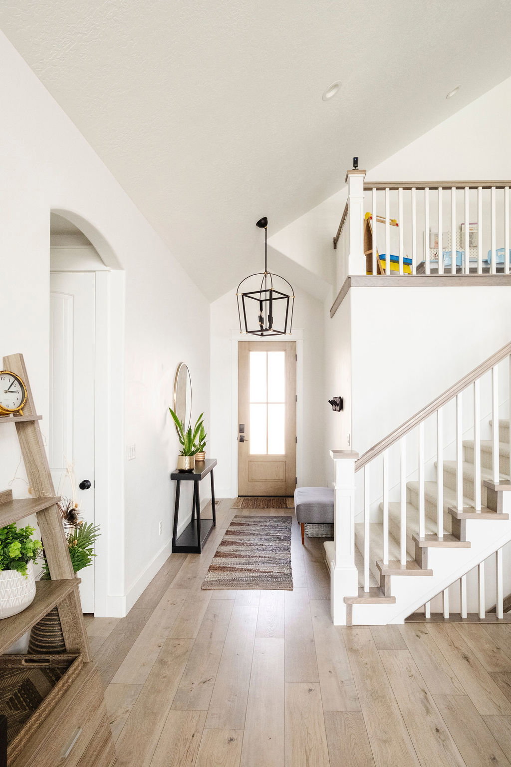 Vaulted entryway with wood-finish flooring, a light wood front door, and a black-framed pendant light fixture