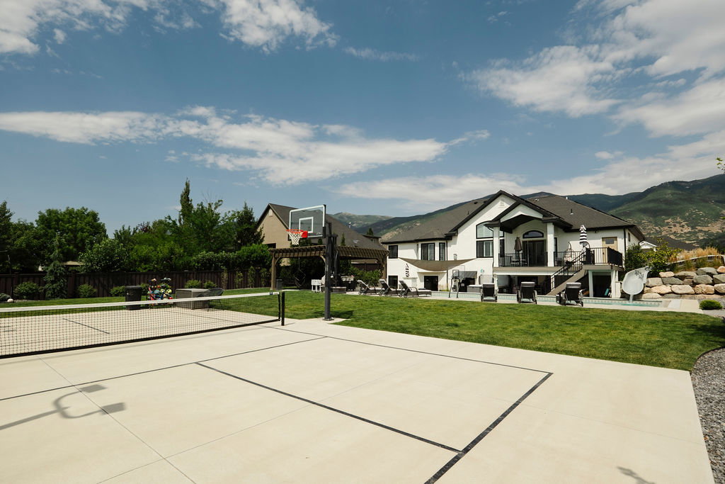 Expansive backyard featuring a multi-sport court with basketball hoop and net, manicured lawn, and mountain backdrop