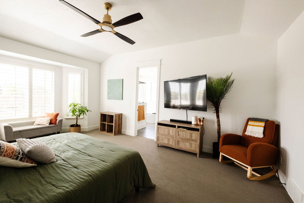 Spacious room featuring vaulted ceilings, a contemporary ceiling fan with a brass finish, and a wide bay window with integrated plantation shutters