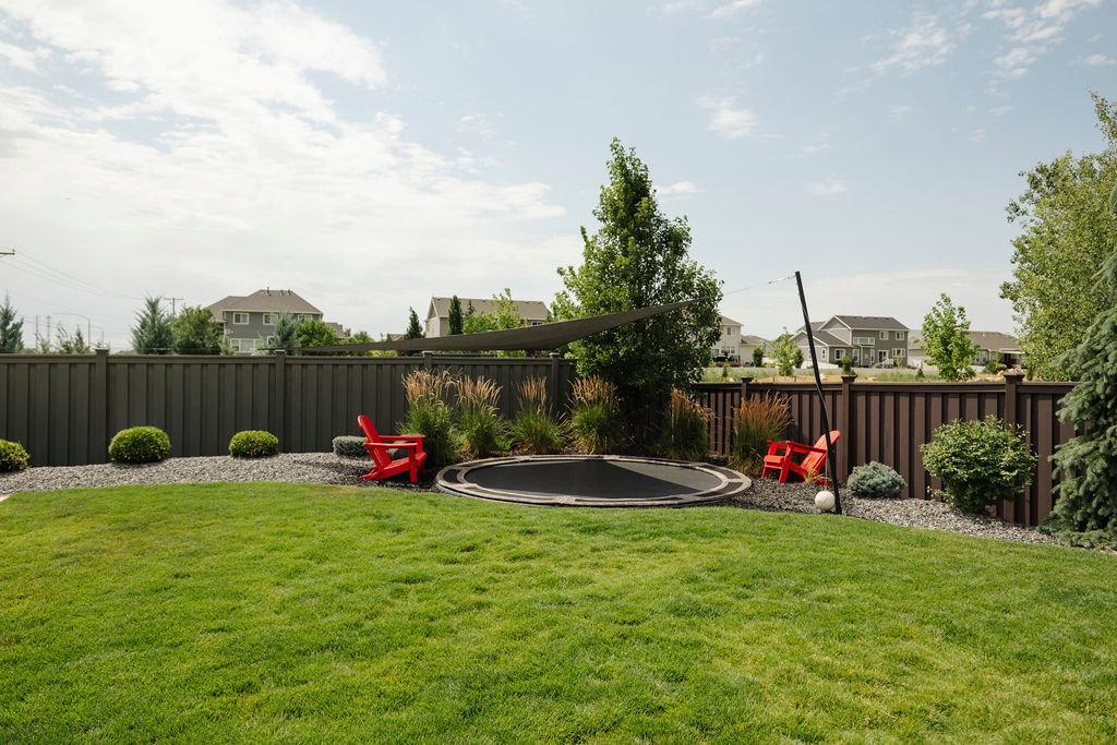 Spacious backyard featuring a manicured lawn, a dark privacy fence, and gravel landscaping