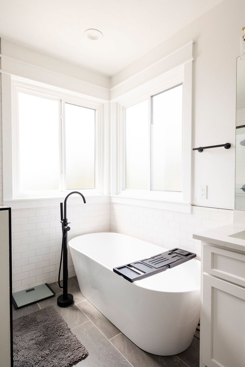 Freestanding soaking tub with a matte black floor-mounted faucet, set against a white subway tile wainscoting