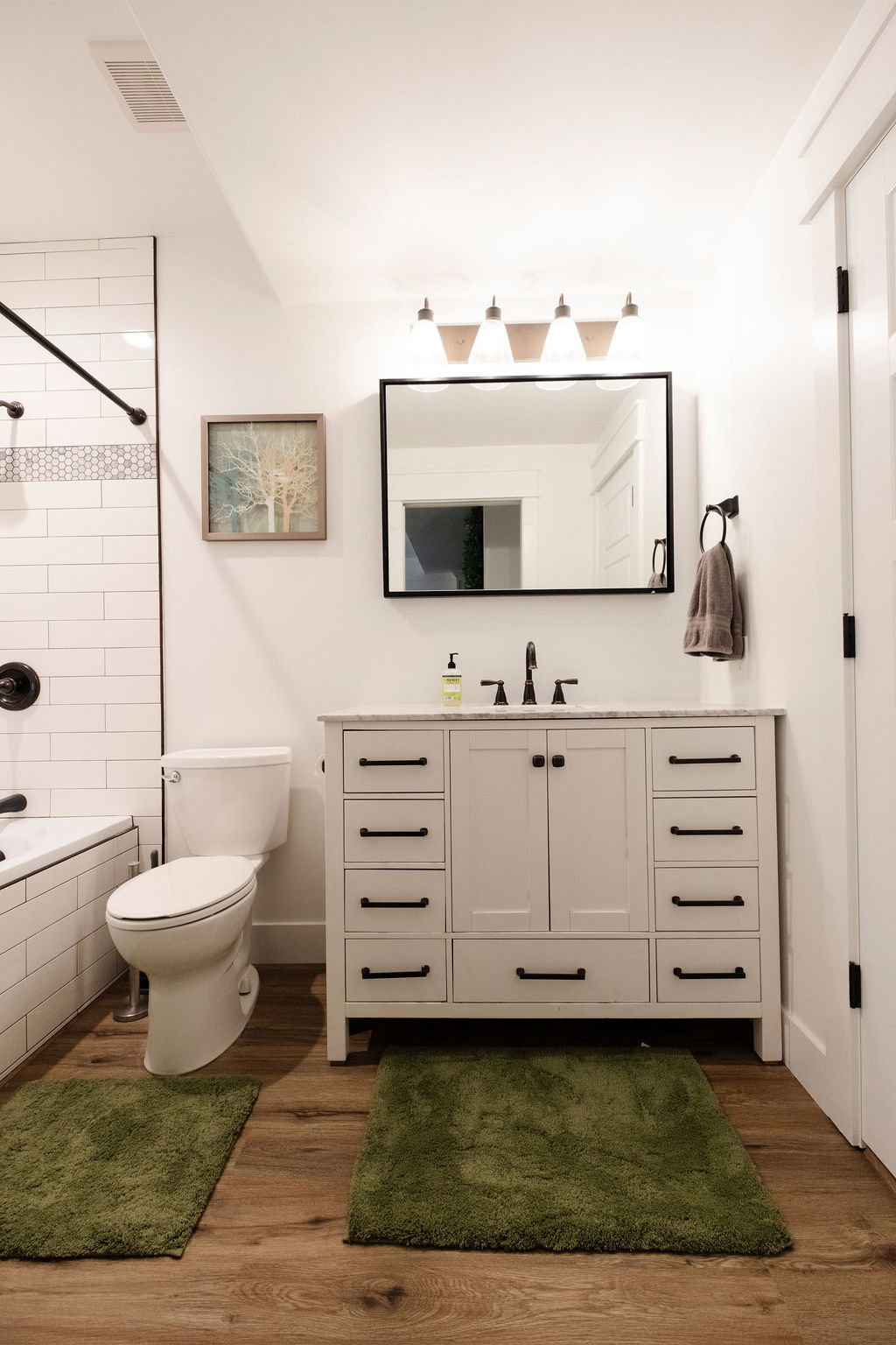 Bathroom featuring a white subway tile shower surround with a decorative accent band, a built-in bathtub, a white vanity with multiple drawers and cabinet storage, a white countertop, and wood-finish flooring
