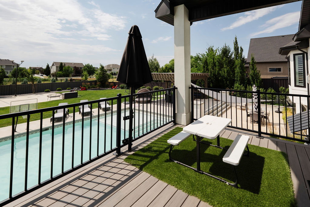 Elevated outdoor deck with composite decking and an artificial turf accent, featuring black metal railings and a clear view of the in-ground swimming pool
