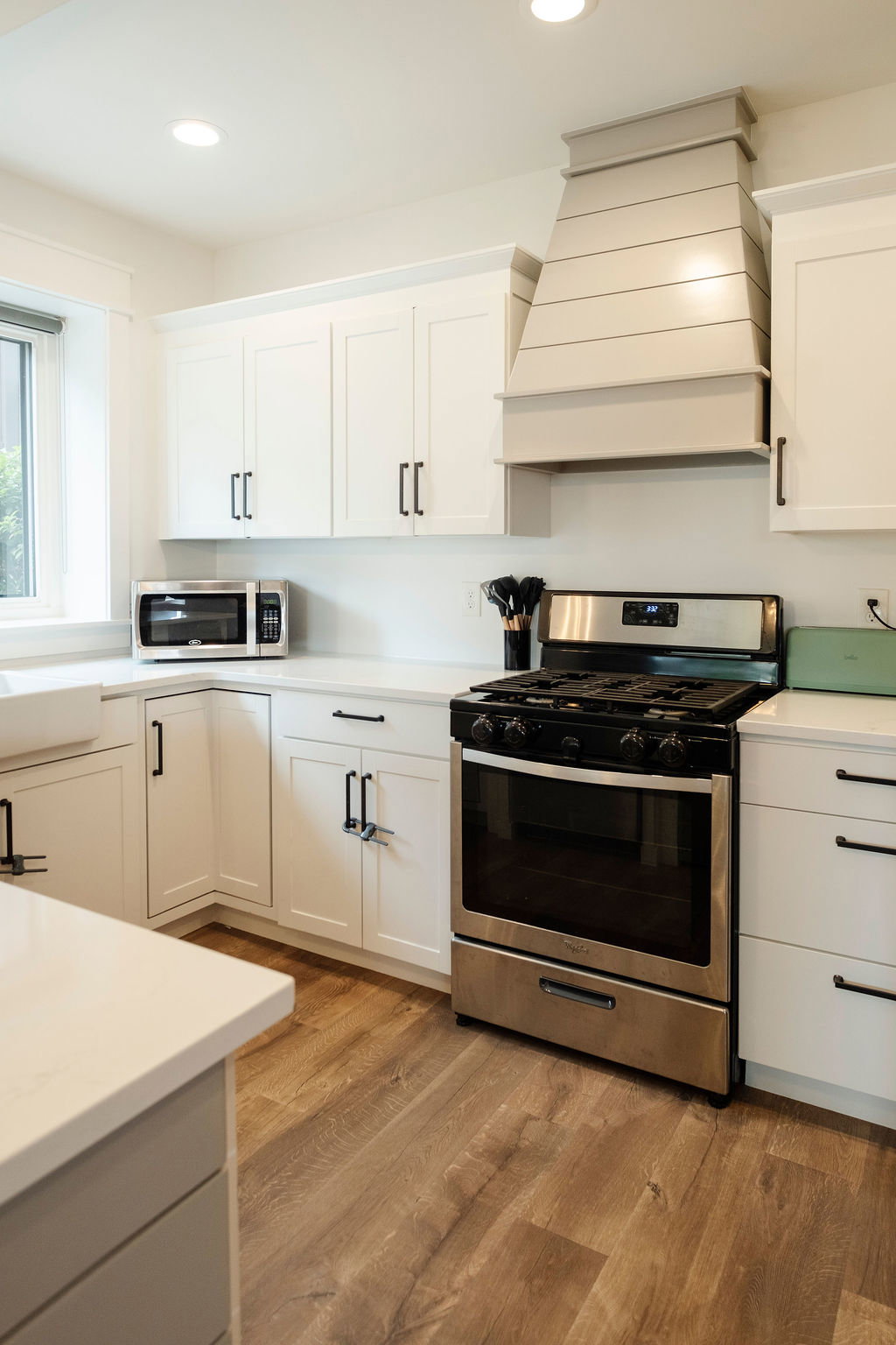 Modern kitchen featuring a stainless steel range, custom range hood, recessed lighting, white cabinetry with dark hardware, and wood-finish flooring