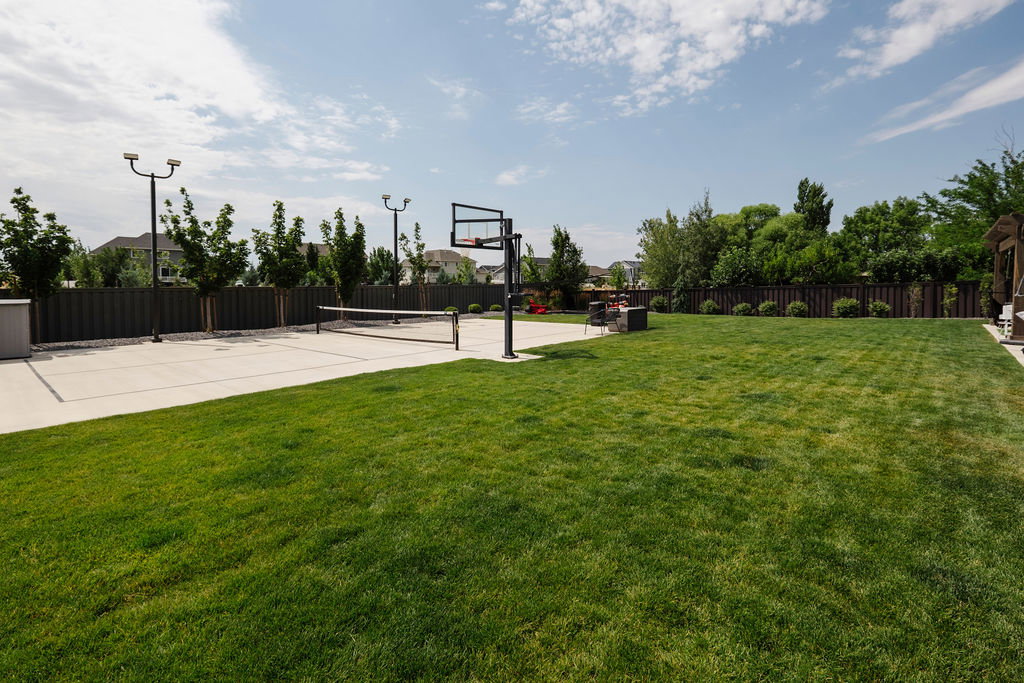 Expansive lawn area with a concrete sports court featuring a basketball hoop and volleyball net