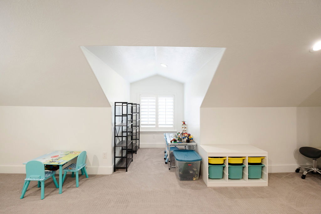 Bright attic space featuring a dormer window with louvered shutters, sloped ceilings, recessed lighting, and neutral carpeting