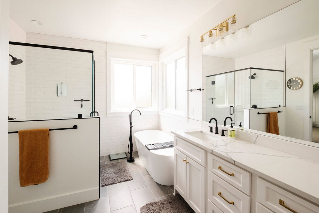 Modern bath featuring a freestanding soaking tub, a separate glass-enclosed shower with subway tile, a dual-sink vanity with quartz countertops, and gold-finish hardware