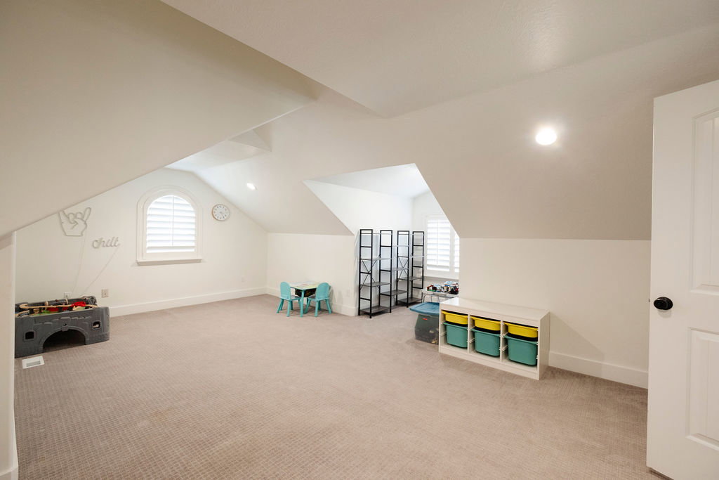Spacious room featuring vaulted ceilings, neutral carpeting, and white walls