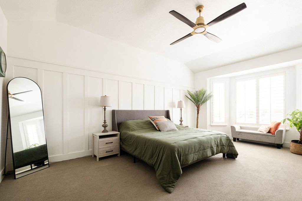 Room featuring a bay window with plantation shutters, board and batten wall accent, and a ceiling fan with integrated lighting