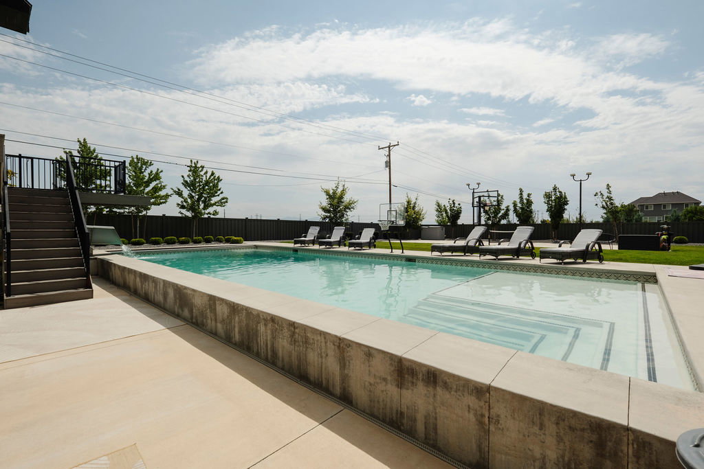 Expansive outdoor pool area featuring a concrete deck, integrated steps, and a perimeter fence