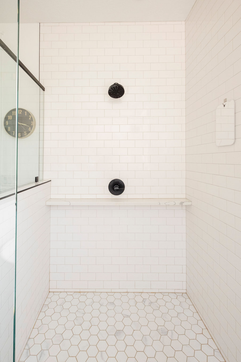 Shower stall featuring white subway tile walls, hexagonal floor tiles, and a built-in shelf