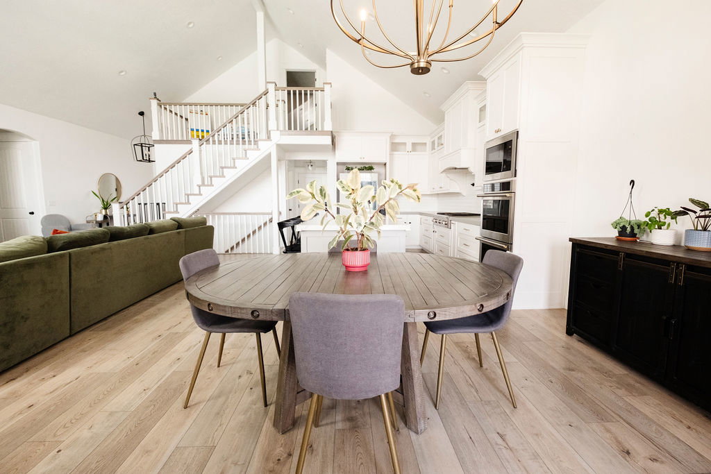 Open-concept interior featuring light wood-finish flooring, vaulted ceilings, and a striking staircase with white risers and railings