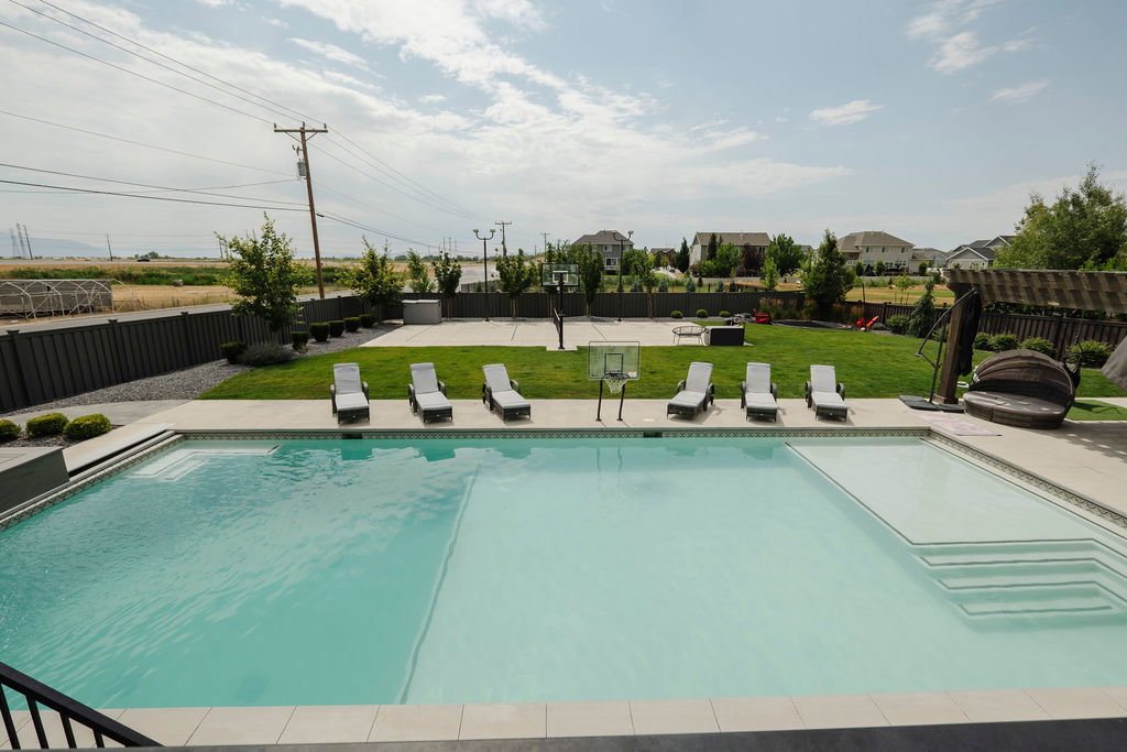 Expansive backyard featuring a large in-ground swimming pool with integrated steps, a concrete pool deck, and a spacious lawn