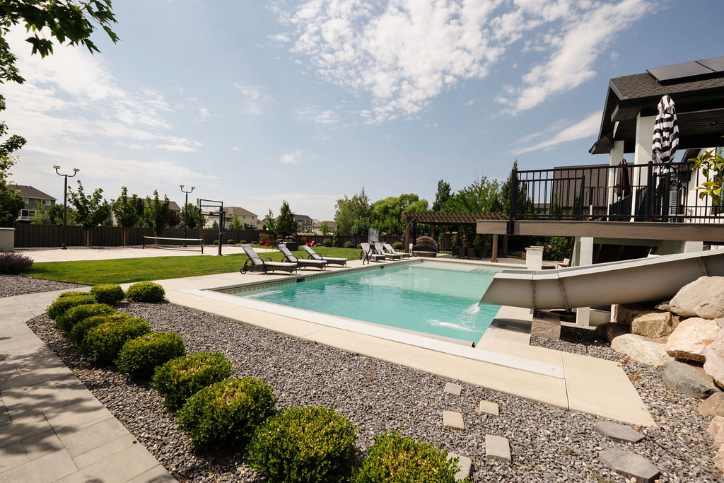 Rectangular swimming pool with integrated slide, surrounded by a concrete patio and grey gravel landscaping