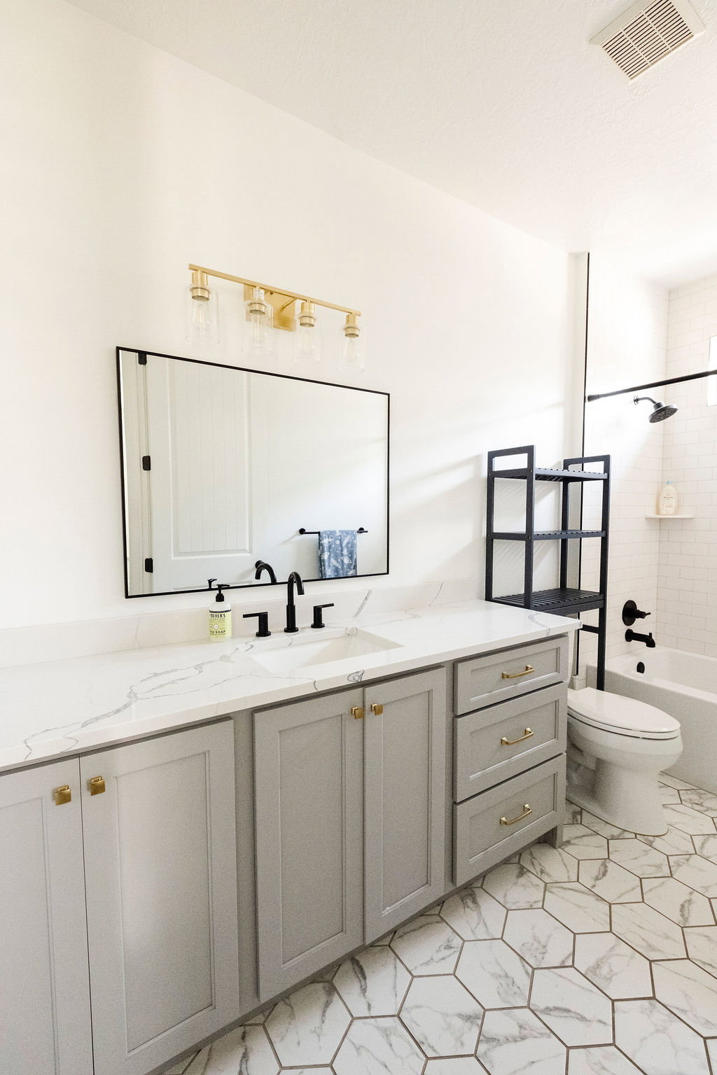 Bathroom featuring a wide vanity with light grey cabinetry, gold hardware, and a white countertop