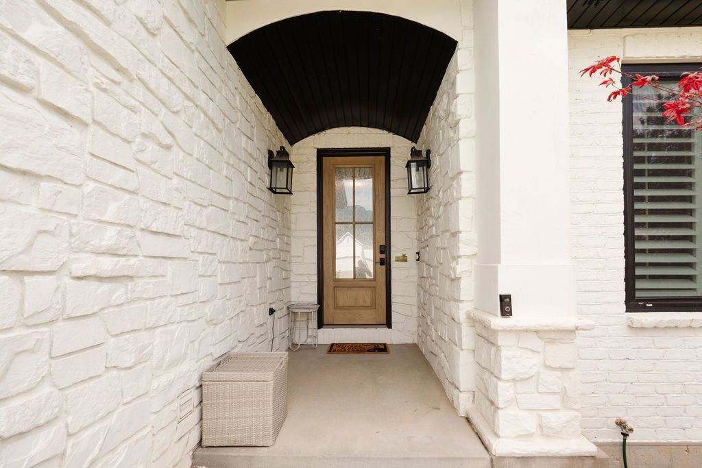 Covered entry featuring a natural wood-finish door with glass panels, white stone veneer siding, and a dark arched soffit