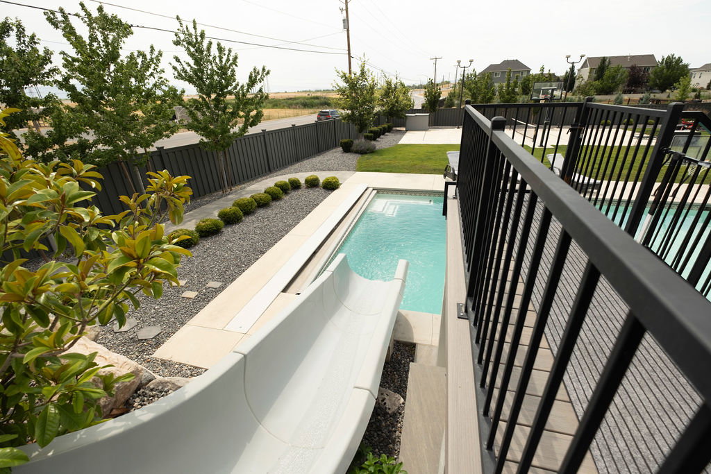 Outdoor living area featuring a swimming pool with a slide, an expansive lawn, a patio area, and mature landscaping
