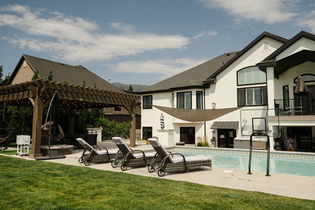 Expansive backyard featuring a large swimming pool, surrounding concrete patio, and a substantial wooden pergola