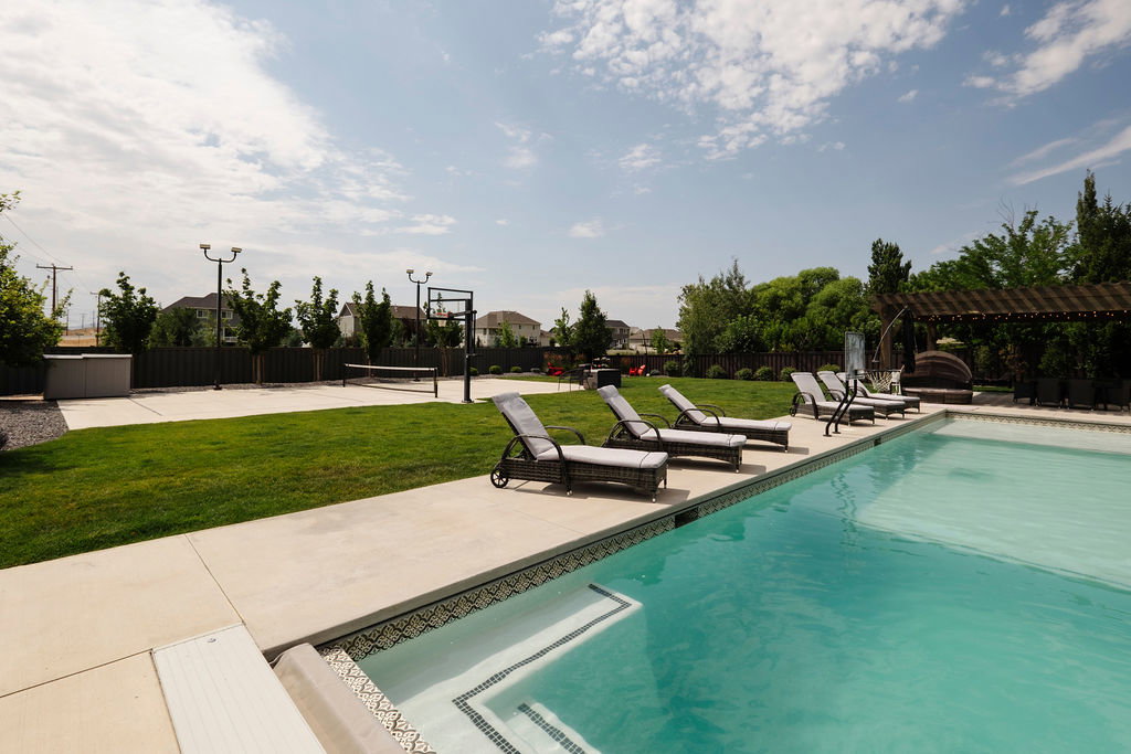 Outdoor swimming pool with integrated steps, surrounded by concrete patio and a manicured lawn