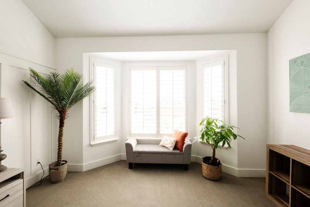 Bay window with plantation shutters and a window seat, light-colored carpeting, white baseboards, and panel accent wall