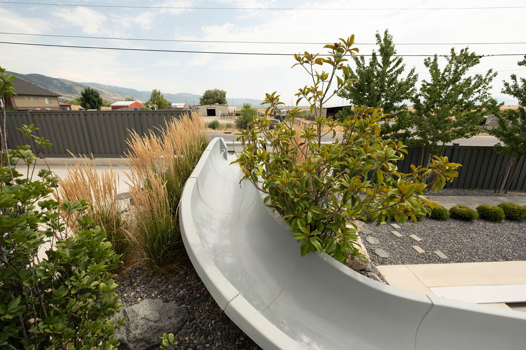 Outdoor space featuring a gray slide, decorative gravel, stepping stones, and mature plantings
