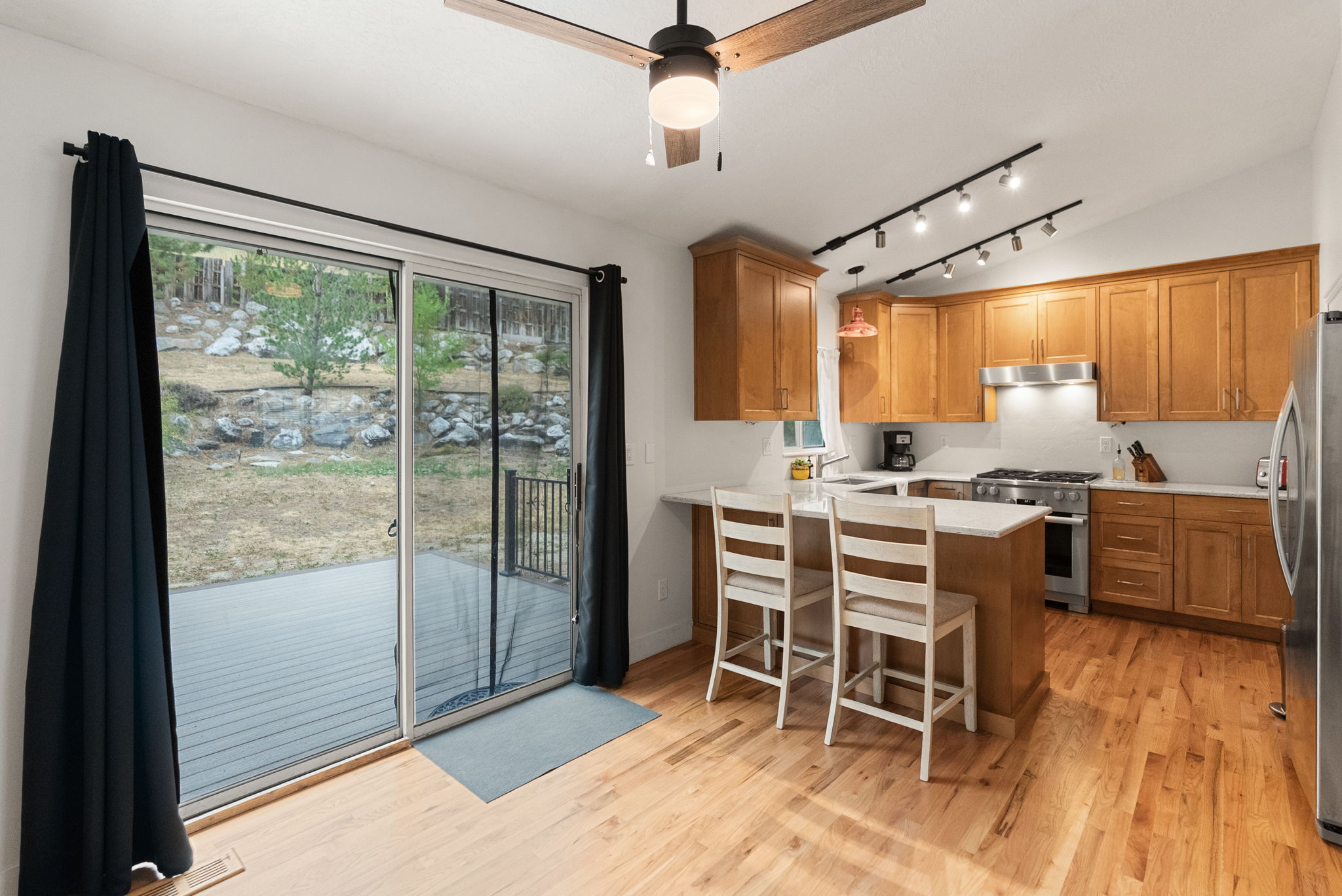 Kitchen and dining area featuring wood-finish flooring, light-toned wood cabinetry, stainless steel appliances, and track lighting