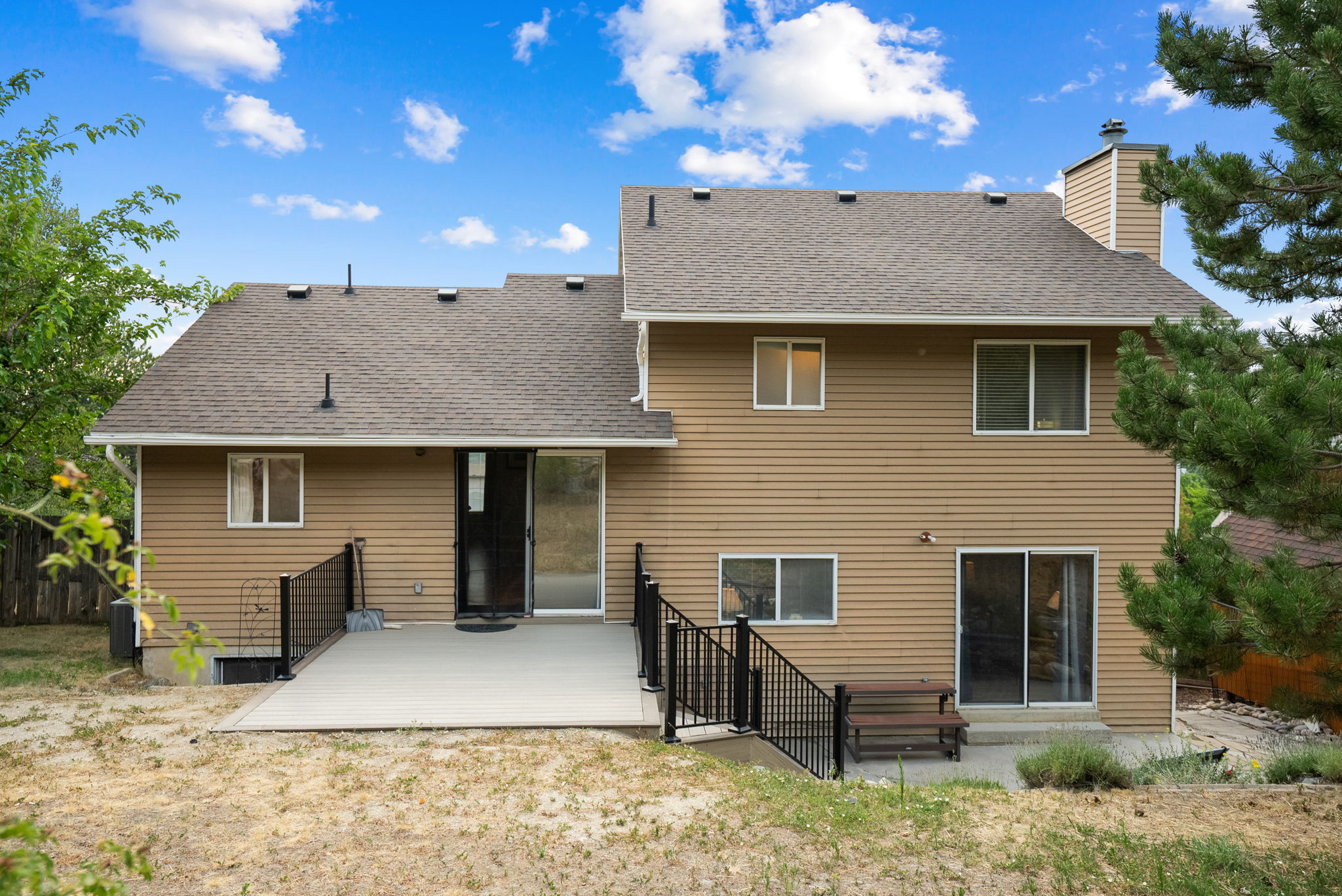 Rear exterior featuring an expansive deck with black metal railings, a sliding glass door entry, and tan horizontal siding