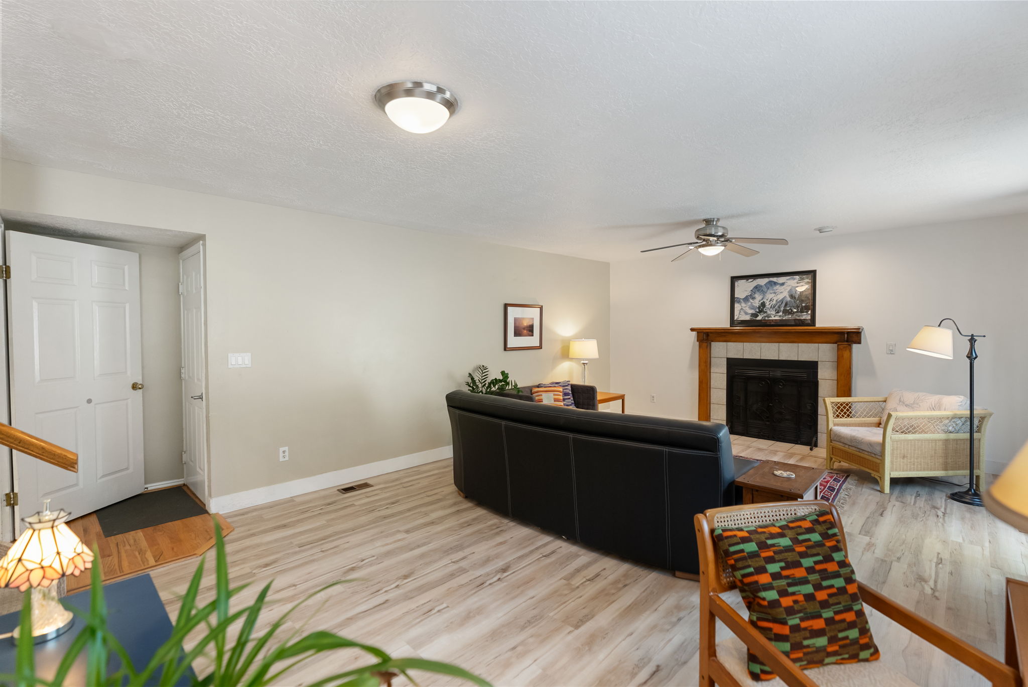 Living area featuring light-toned wood-finish flooring, a ceiling fan with integrated lighting, and a fireplace with a wood mantel and tile surround