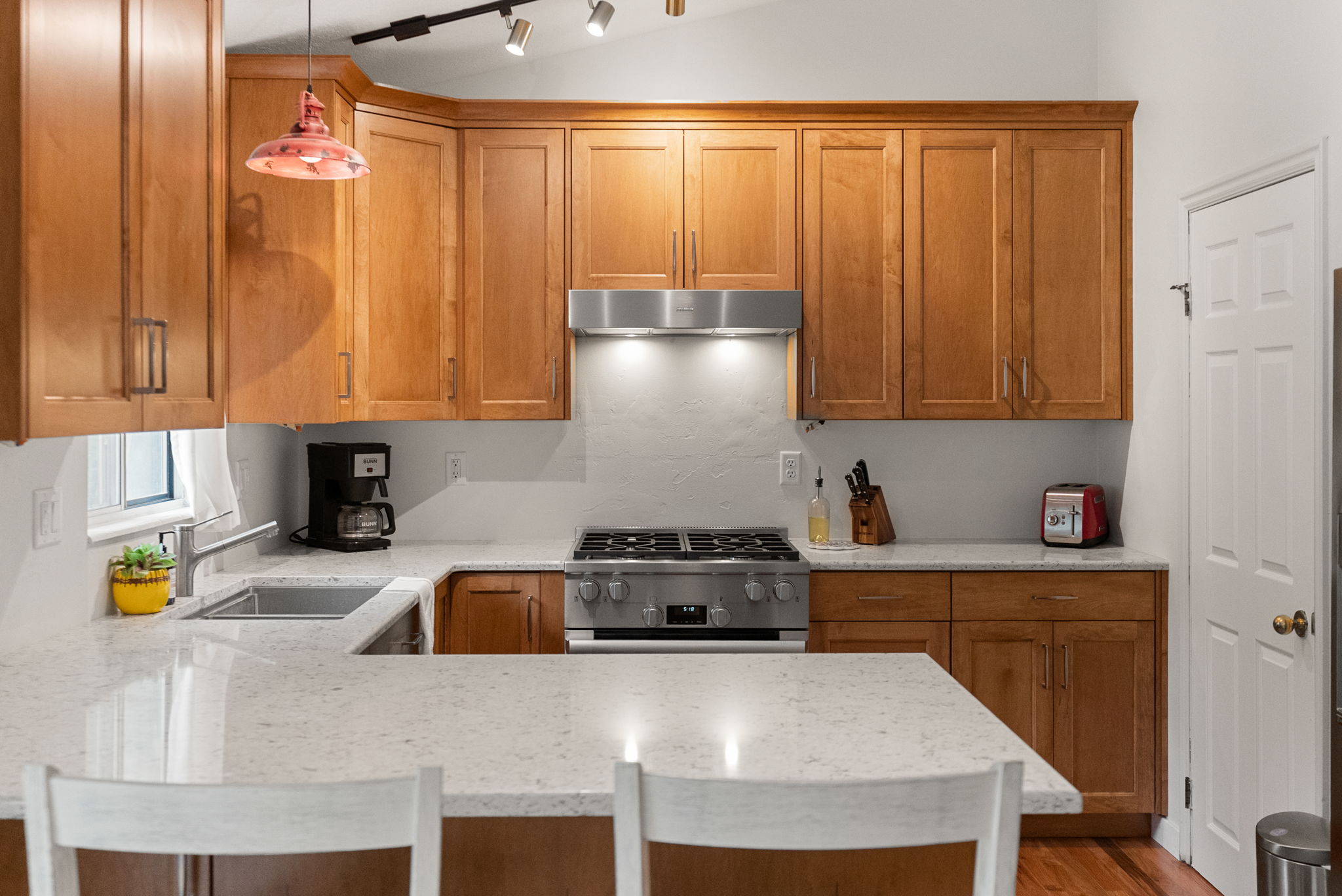 Contemporary kitchen featuring wood cabinetry, light-toned countertops, a stainless steel gas range, and a coordinating stainless steel range hood