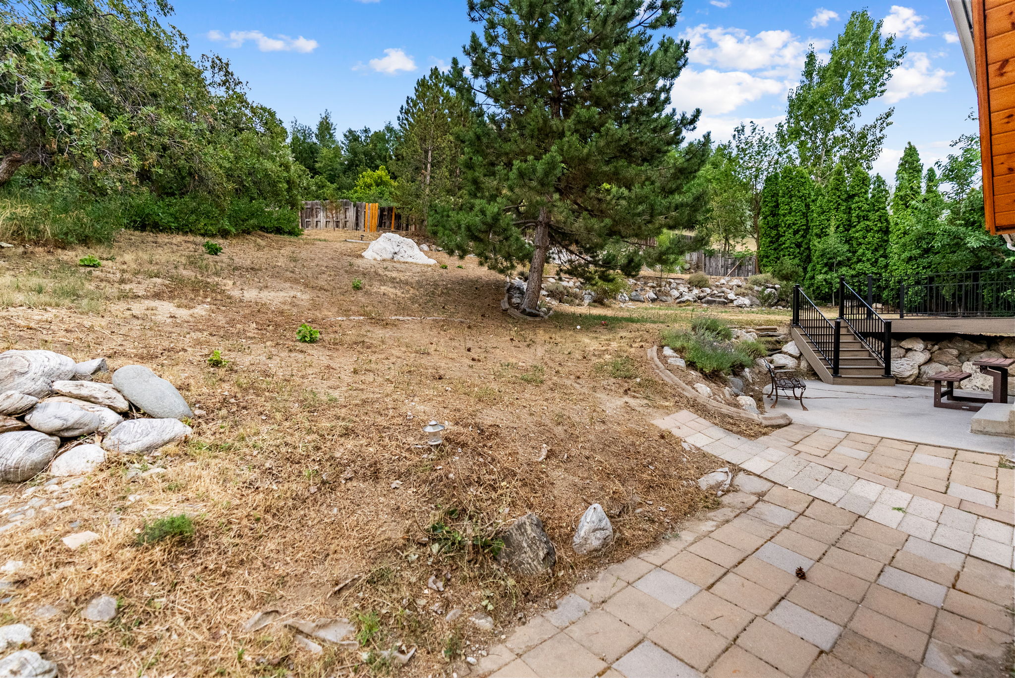 Expansive terraced backyard featuring a paver patio, multi-level wooden deck with black railings, and mature trees