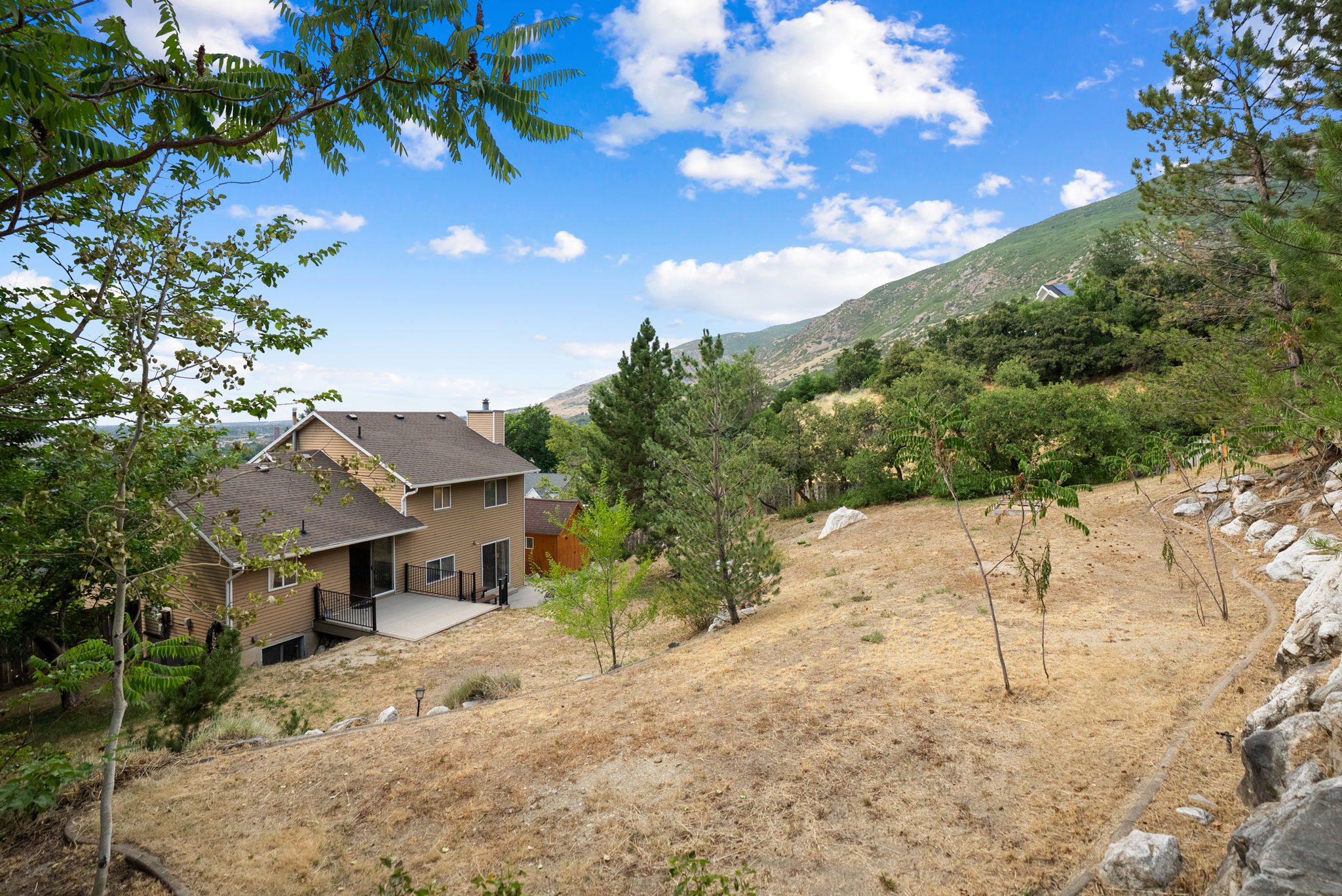 Hillside property featuring a multi-level home with a neutral stucco exterior, a dark shingle roof, and a spacious deck