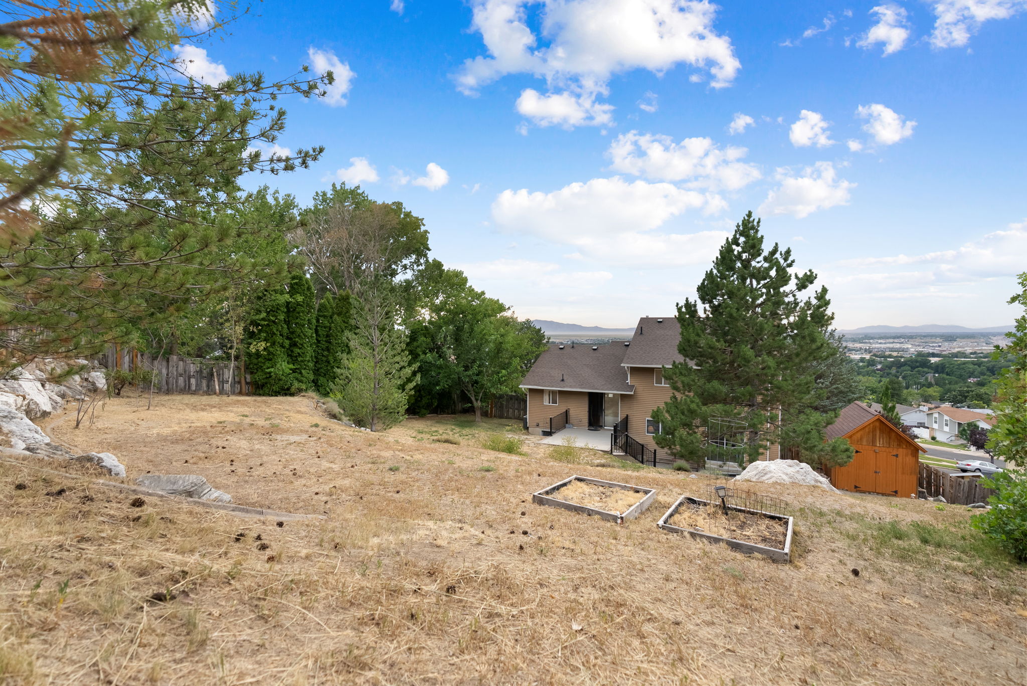 Expansive sloped property featuring a stucco-sided residence, a wooden shed, and elevated garden beds
