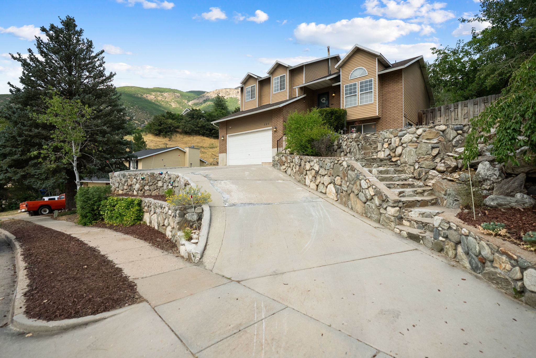 Split-level residence featuring a two-car garage, brick and stucco exterior, arched windows, and a multi-tiered stone retaining wall