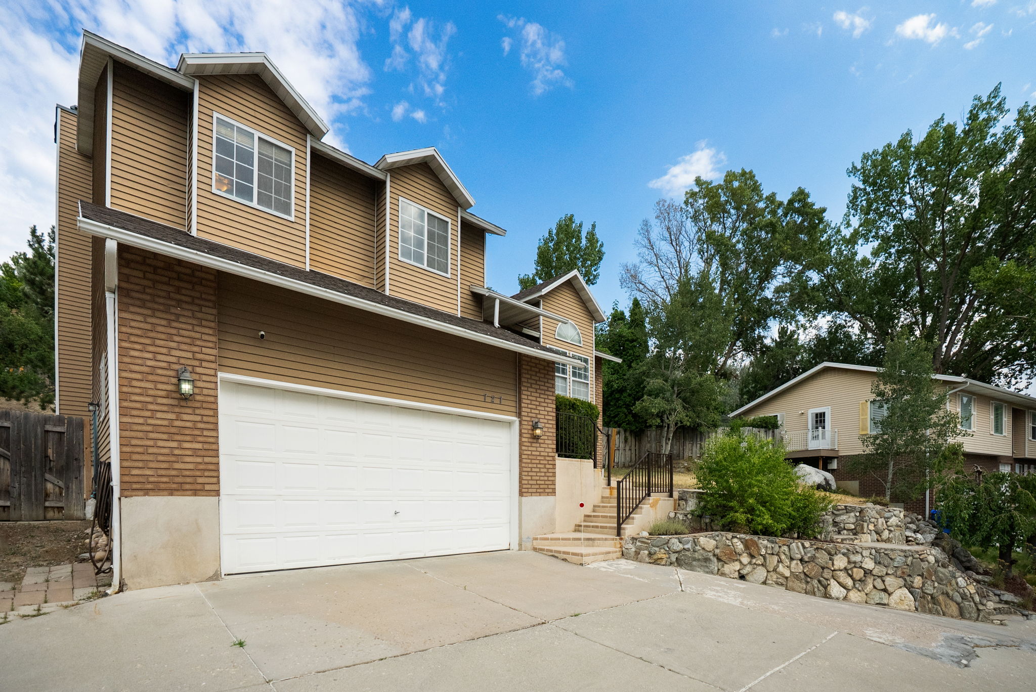 Multi-level residence featuring a two-car garage with a white door, light brown brick, and horizontal siding