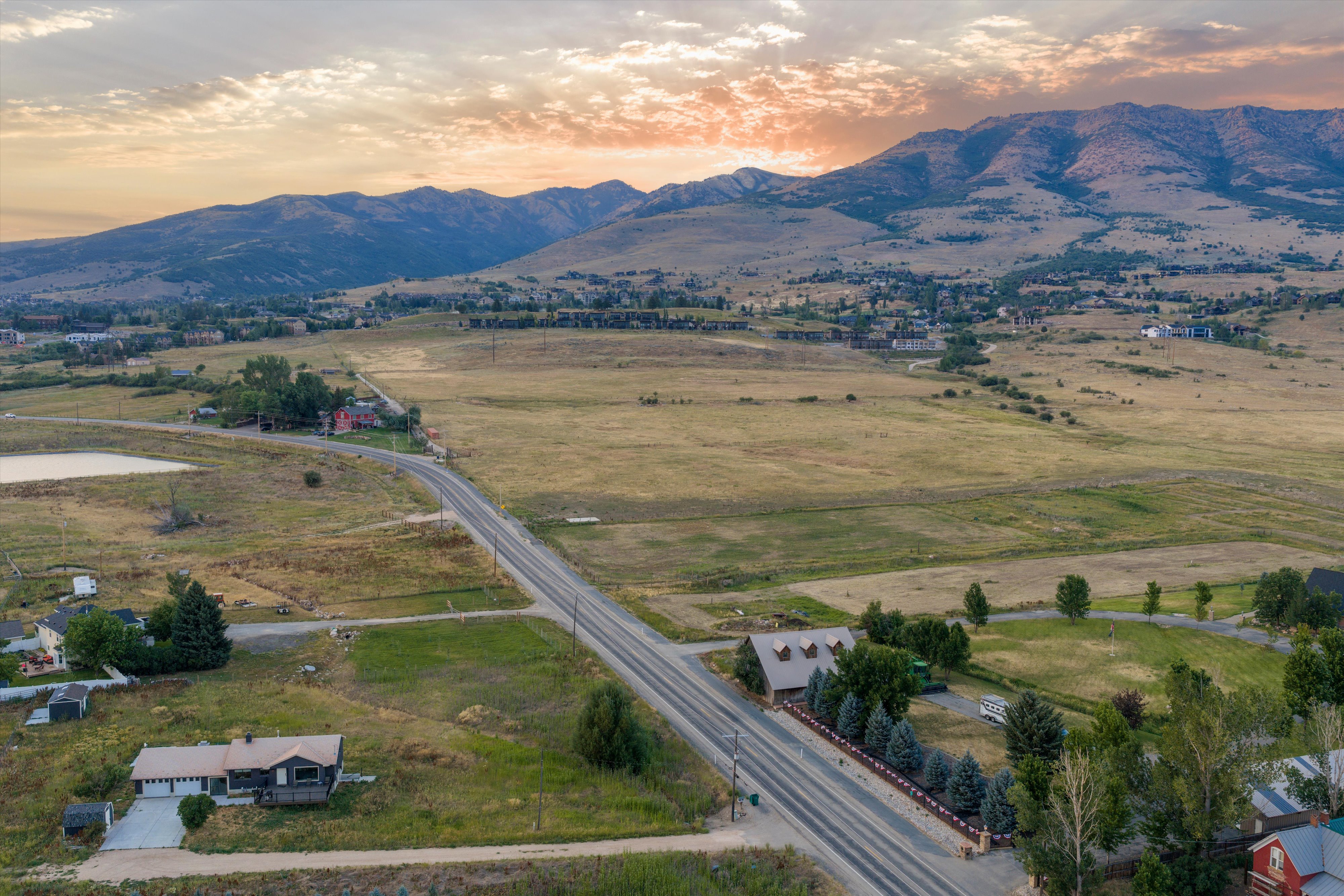 Expansive mountain landscape with a meandering roadway, scattered residential properties, and a prominent pond