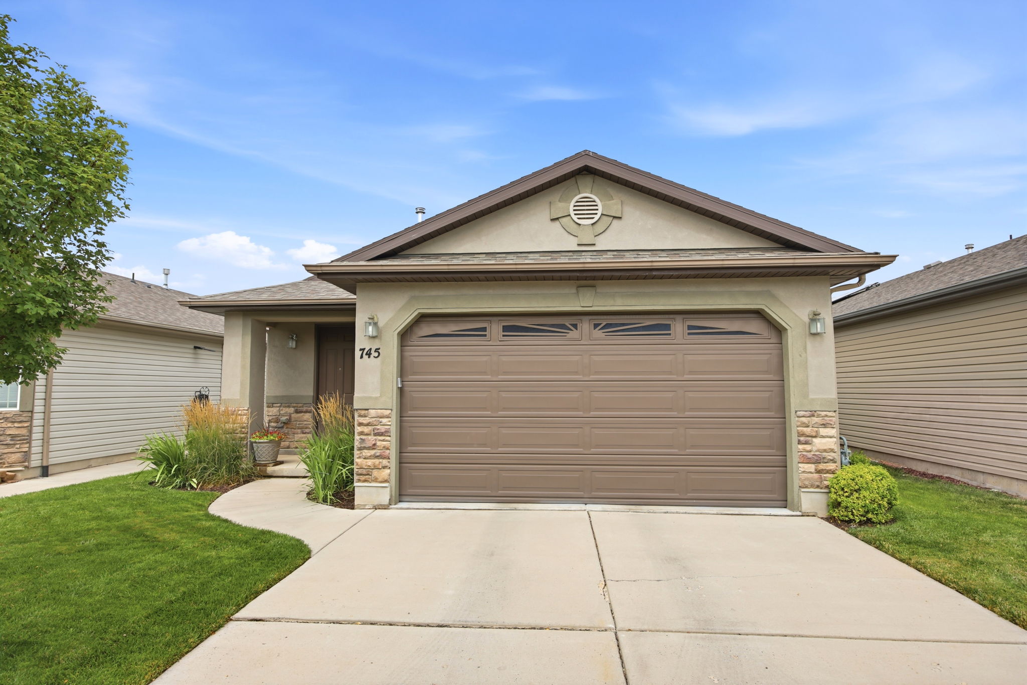 Exterior facade featuring a brown garage door with window inserts, stucco siding, and stone accents