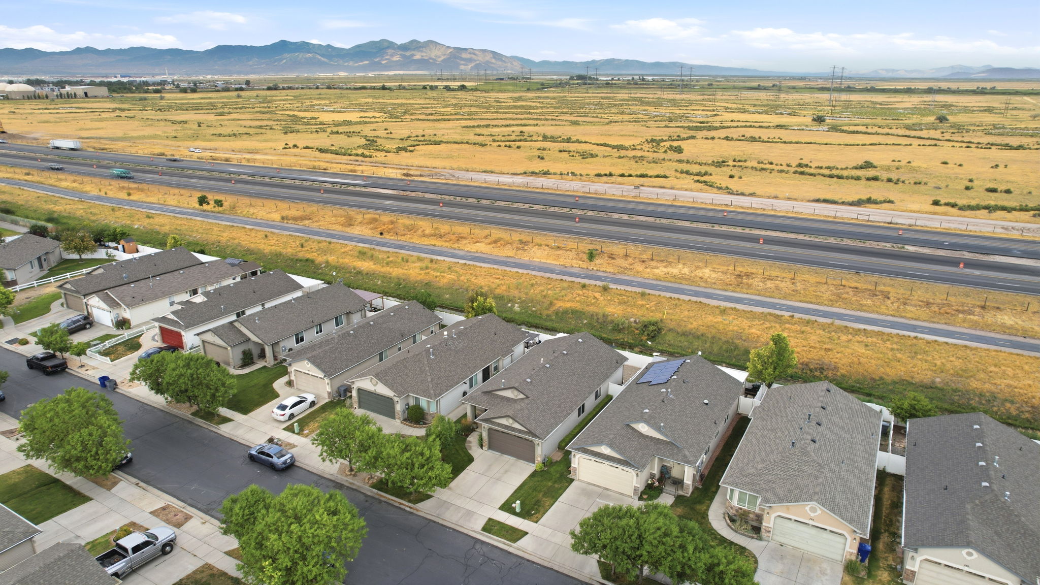 Aerial perspective showcasing a residential street with single-story homes, a multi-lane highway, and expansive arid terrain
