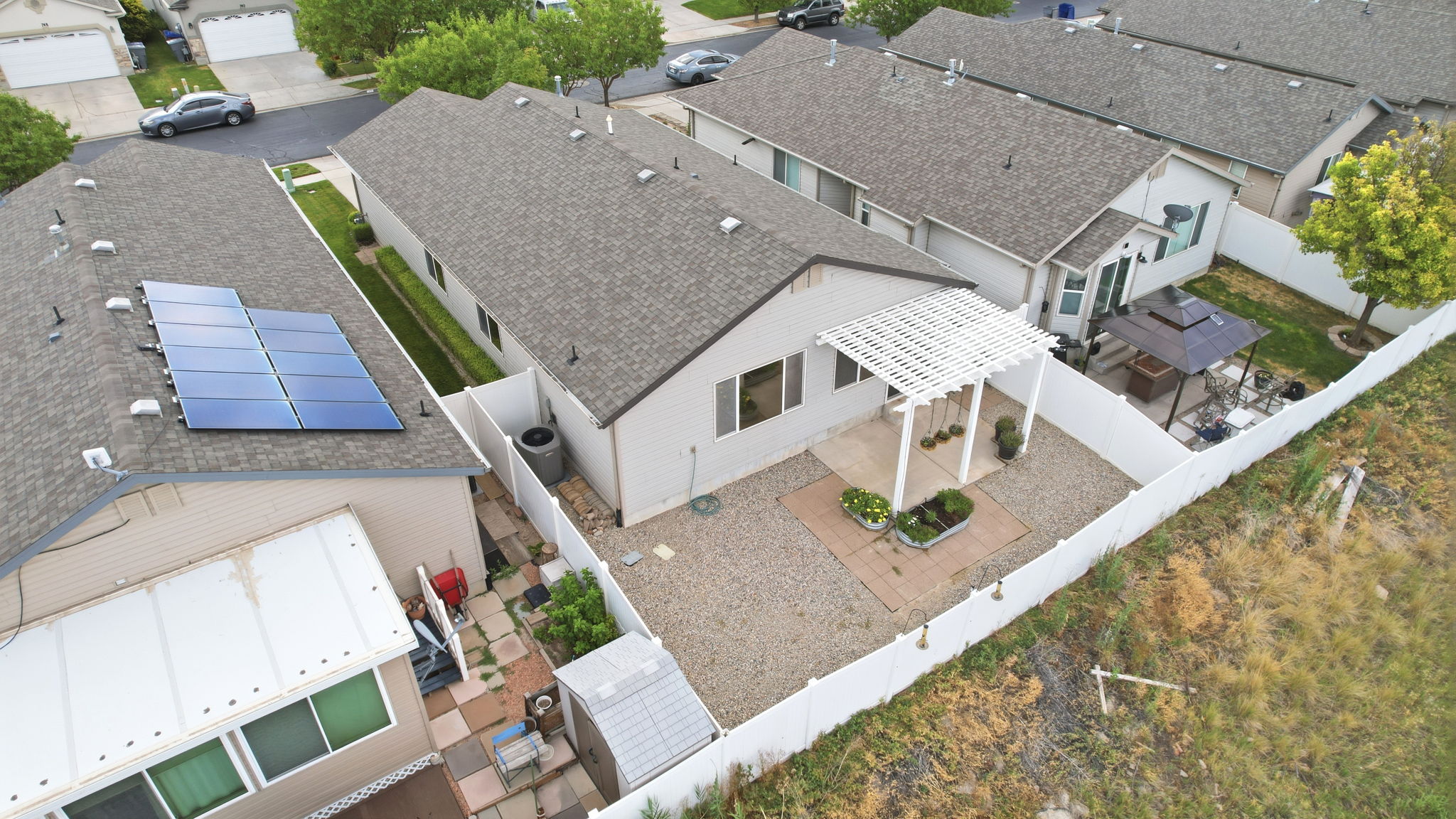 Low-maintenance backyard featuring a white lattice pergola, gravel patio area, privacy fencing, and a separate paved side yard