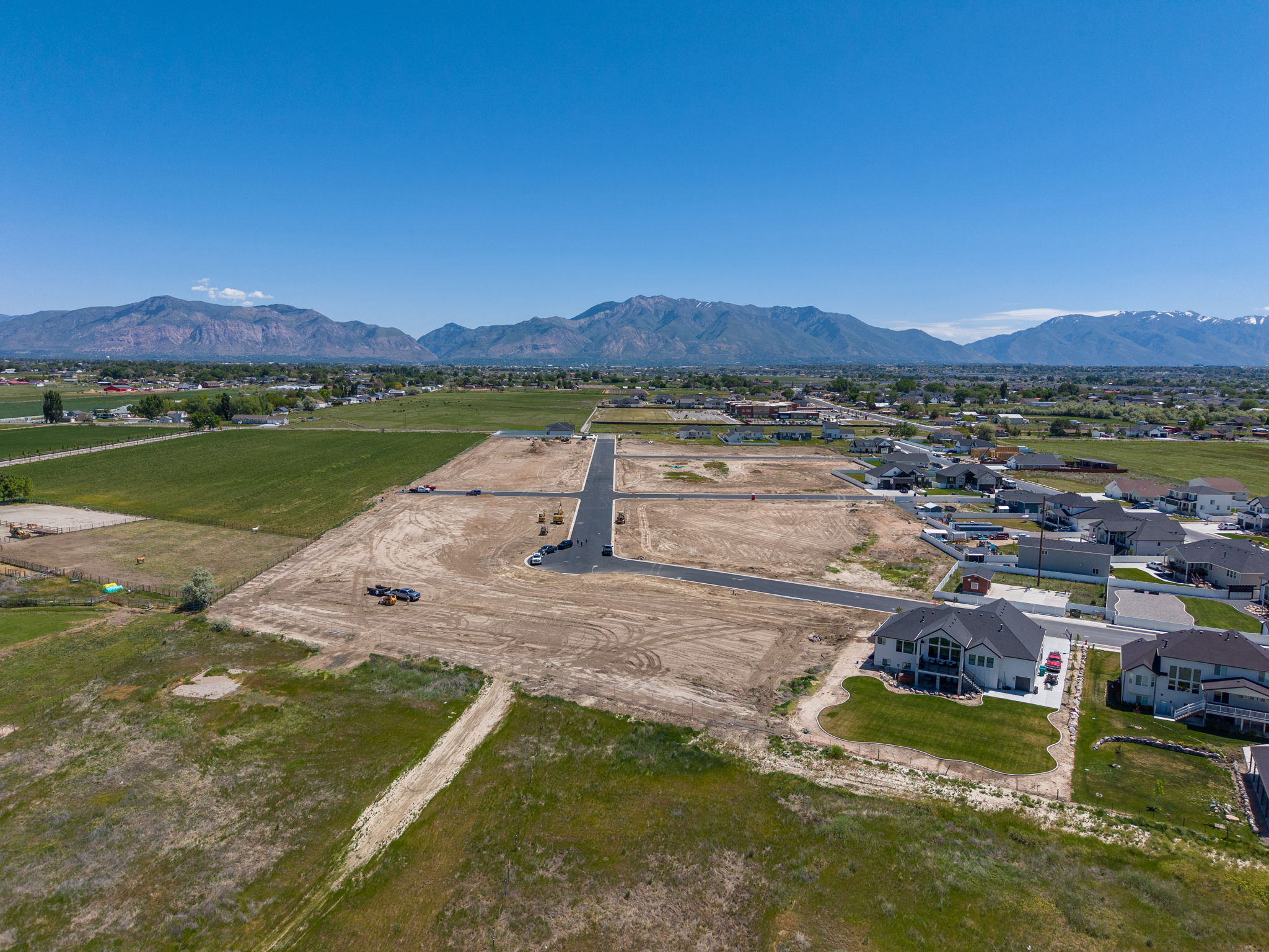 Expansive undeveloped land with mountain backdrop, surrounded by established residential areas and agricultural fields, featuring existing paved road infrastructure
